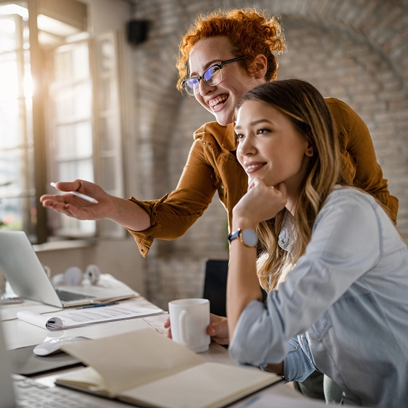 insurance-agency-2-compressed Young happy businesswomen cooperating while using desktop PC in the office.